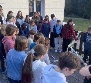 Eine Gruppe von Kindern und Jugendlichen stehen auf einer Terrasse und betrachten eine Konstruktion aus Papier und Klebeband.