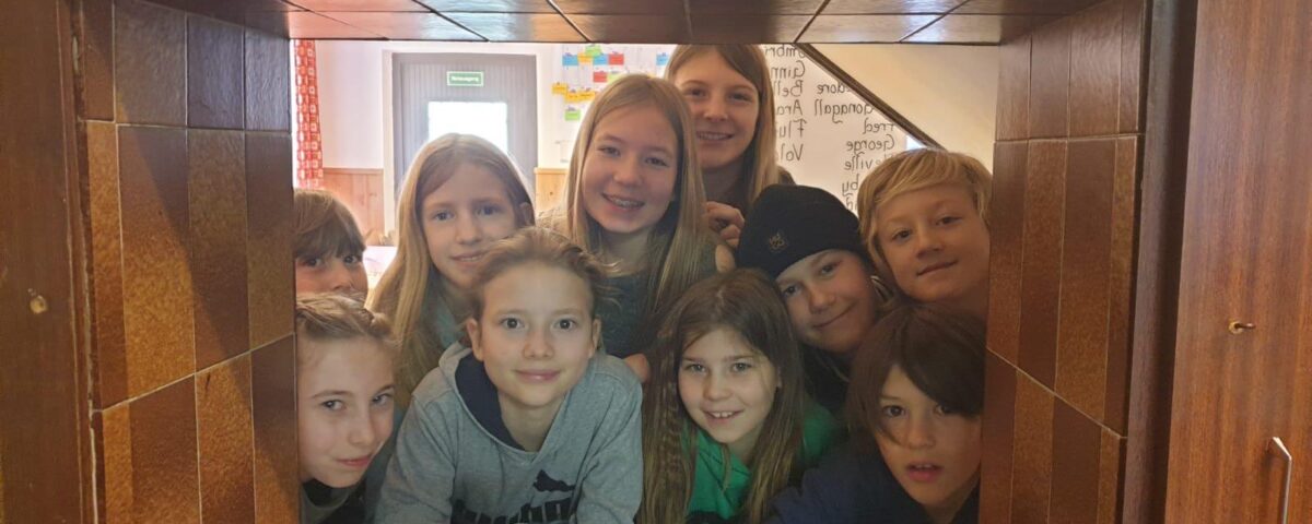 Gruppe von Kindern schaut interessiert und lächelnd durch eine Öffnung in der Wand.