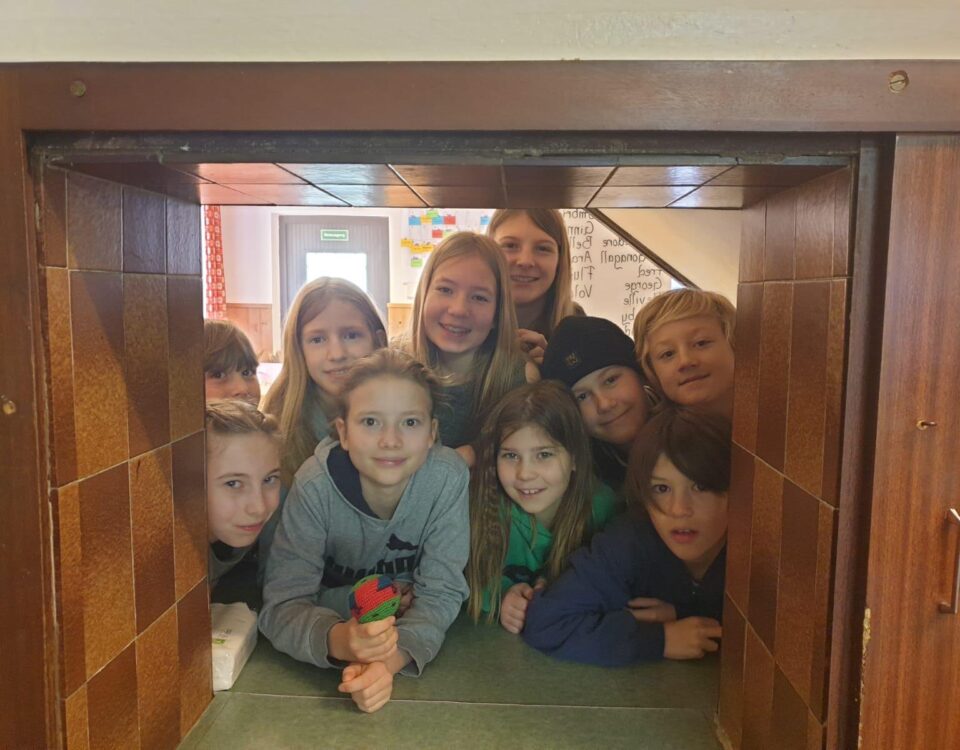 Gruppe von Kindern schaut interessiert und lächelnd durch eine Öffnung in der Wand.