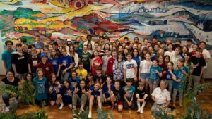 Gruppenbild von einem CISV PreCamp-Wochenende. Große bunte Gruppe vor buntem Hintergrund